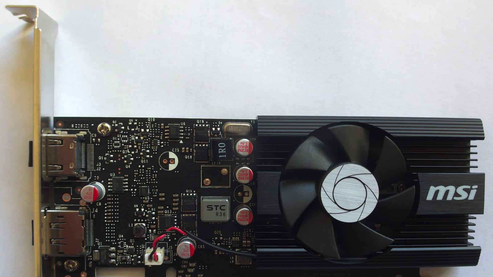 A low-profile MSI GeForce GT 1030 graphics card photographed flat, showing its circuit board, a small fan cooler and two display outputs.